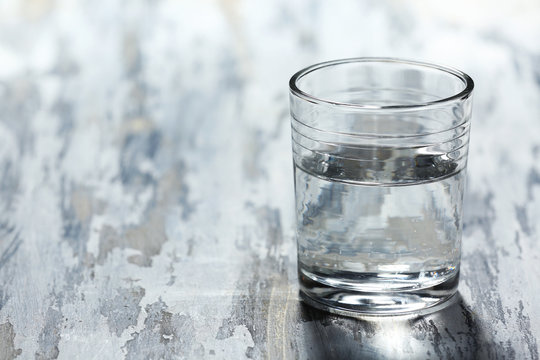 Glass of clean mineral water on old color wooden background