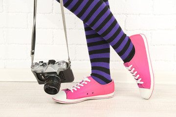 Girl in sneakers with retro photo camera in room
