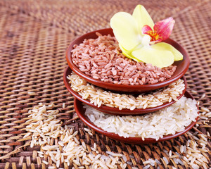 Different types of rice in bowls on wicker background