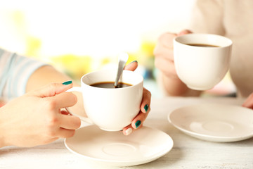 Two women with cups of coffee on bright background
