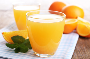 Glasses of orange juice with oranges on wooden table close up