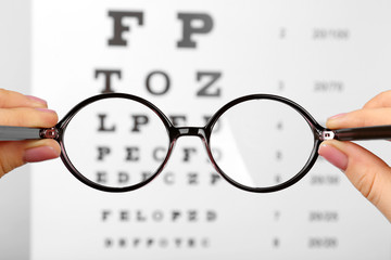 Glasses in hands on eye chart background, close-up © Africa Studio