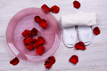 Spa bowl with water, rose petals, towel and slippers