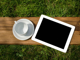 tablet and blank coffee cup on green grass