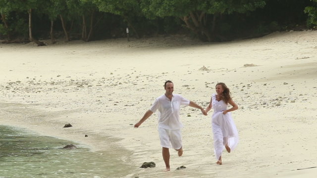 blonde bride and handsome groom running along sandy beach