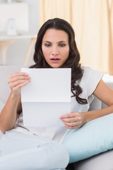 Shocked brunette reading letter on couch