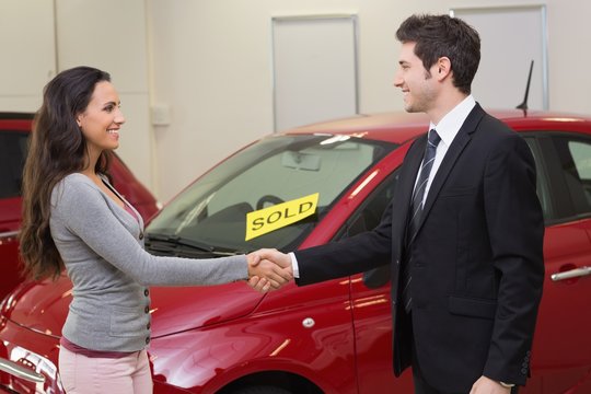 Person shaking hands in front of a sold car