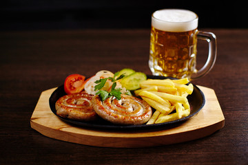 Roasted sausages in a frying pan on wooden table with beer