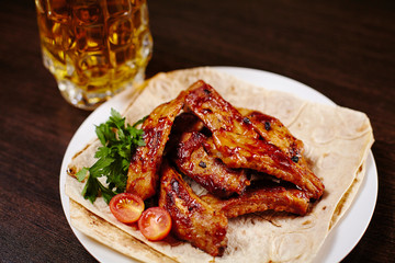 Plate with roasted pork ribs on wooden table