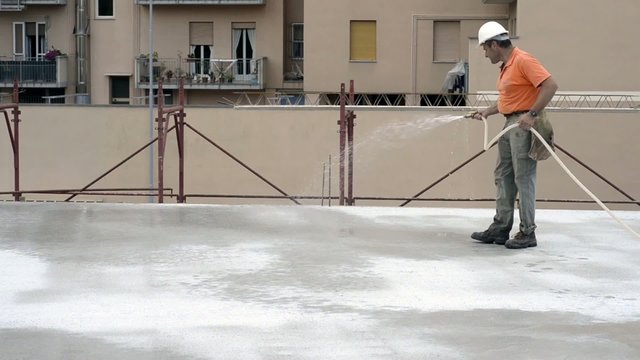 Construction worker watering fresh concrete slab using a hose
