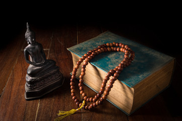 Buddha statue with necklace and antique book. - Powered by Adobe
