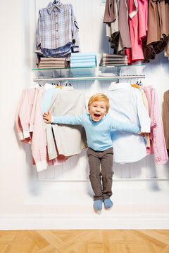 Laughing boy standing among clothes in the shop
