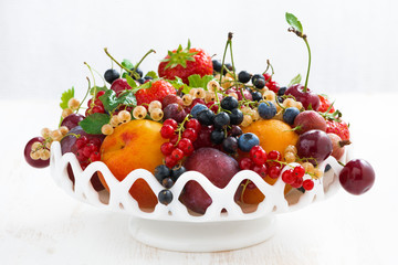 dish with seasonal fruit and berries on white table, close-up