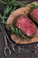 Raw peppered steak with herbs on wooden table