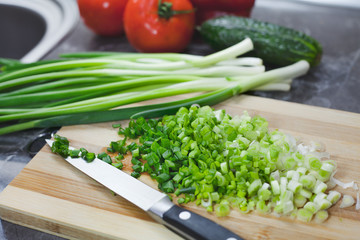 Chopped green onions and vegetables on striped wooden board