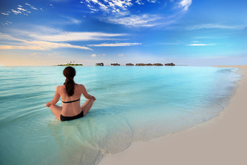 Young woman exercising yoga in turquoise lagoon with overwater b