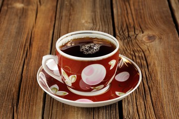 Red cup of black tea with bubbles on wooden background