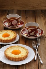 Peach tarts and cups of black tea on wooden background