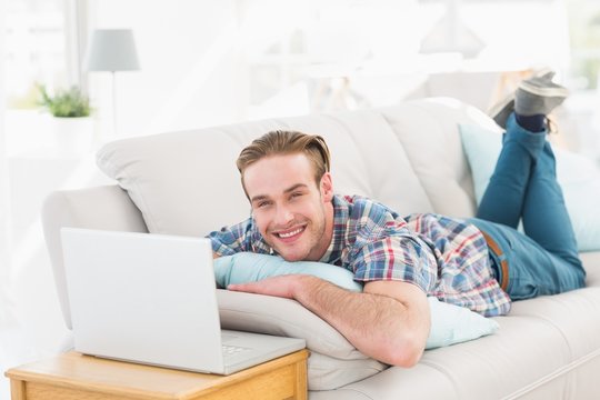Happy man lying on sofa using laptop