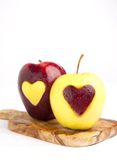 Fresh, wet red & green apples with a heart shaped cut-out on whi