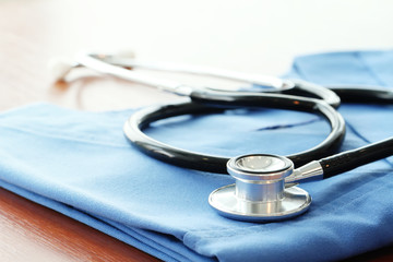 Stethoscope with blue doctor coat on wooden table and  backgroun