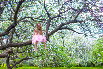 Little adorable girl sitting on blossoming tree in apple garden