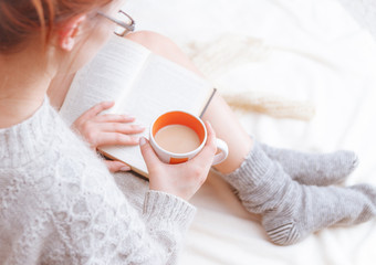 photo of a woman in a sweater with the old book and a cup of tea