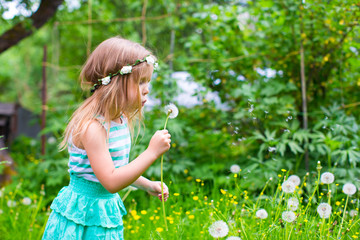 Adorable little girl blowing a dandelion in the garden
