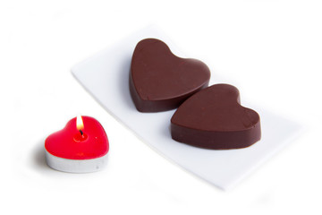 Candle and chocolates in the shape of heart on white background