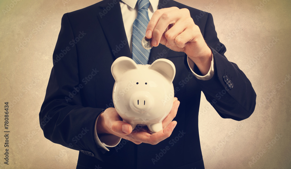 Wall mural young man depositing money in piggy bank