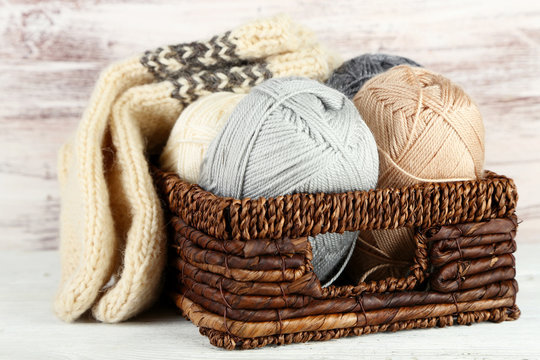 Knitting yarn and socks in basket, on wooden background