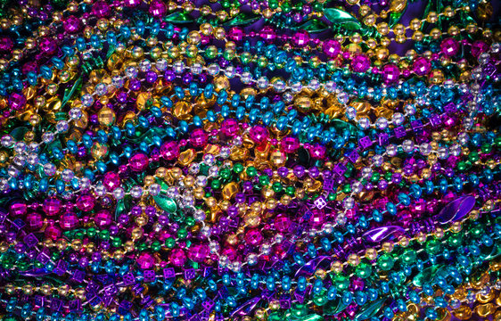 A background of  brightly colored Mardi-Gras beads on a purple b