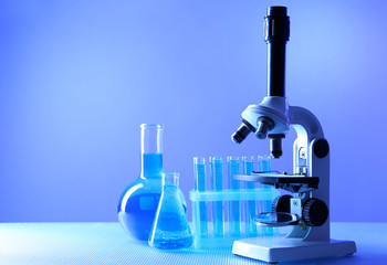 Microscope and test tubes on table, on color background