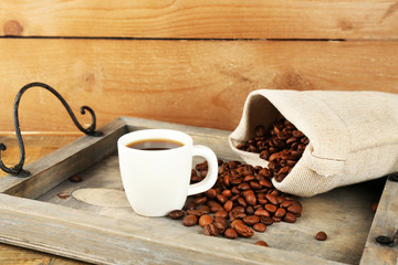 Cup of coffee with beans on tray and rustic wooden background
