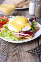 Toast with egg Benedict and tomato on plate on wooden table