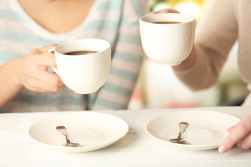 Two women with cups of coffee on bright background