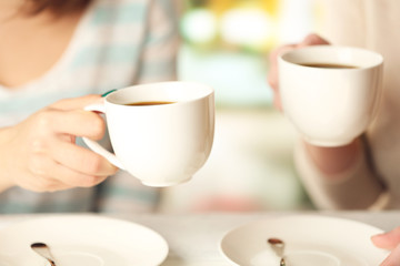 Two women with cups of coffee on bright background