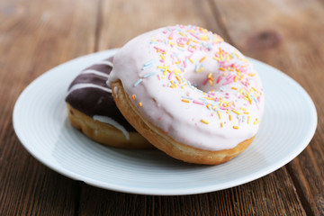 Delicious donuts with icing on plate on wooden background