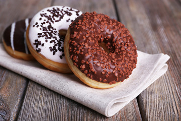 Delicious donuts with icing on napkin on wooden background