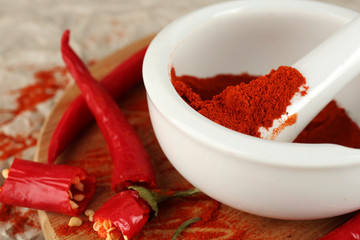 Ground red pepper in mortar with chili pepper on table close up