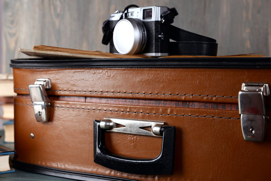 Vintage suitcase with camera on wooden background