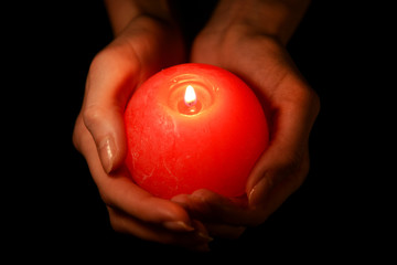 Candle in female hands on black background