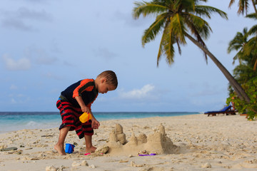 little boy building sand castle on tropical beach