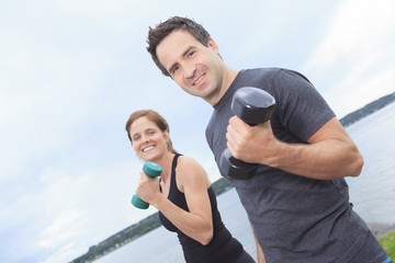 A Young, caucasian couple working out with dumbbells outside