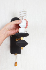 Hand unscrews tungsten bulb in luminaire on a white wall