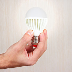 Hand holding a glowing led bulb on a light wood background
