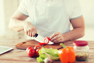 male hand cutting tomato on board with knife