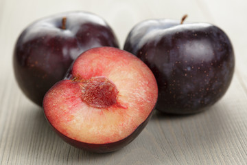 three ripe black plums on wood table
