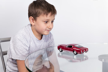 Boy playing with red sports car on a glass table