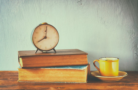 Image of old clock and coffee cup over wooden table. image is fi